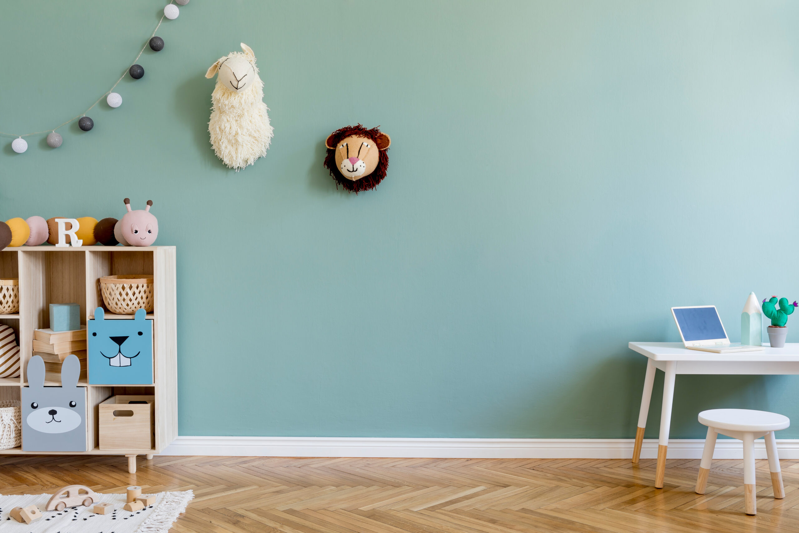 Interior design of scandinavian childroom with wooden cabinet, mint armchair, white desk, a lot of plush and wooden toys. Eucalyptus color of background walls. Plush animal head on the wall. Template Safe painting preparation for kids bedroom