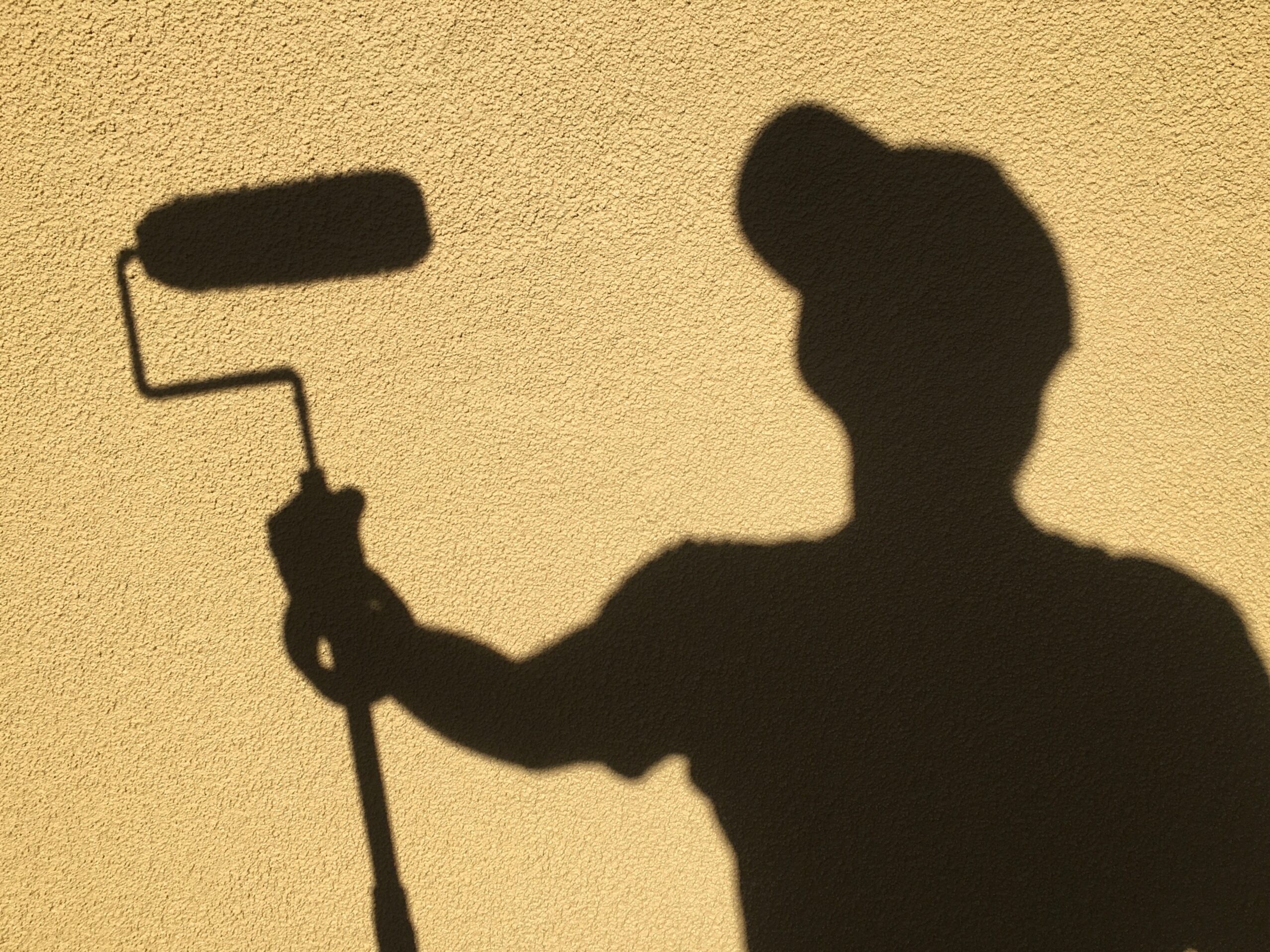 Professional Painter at Work with a Roller Silhouette of a professional painter holding a paint roller against a textured yellow wall, ready to paint.