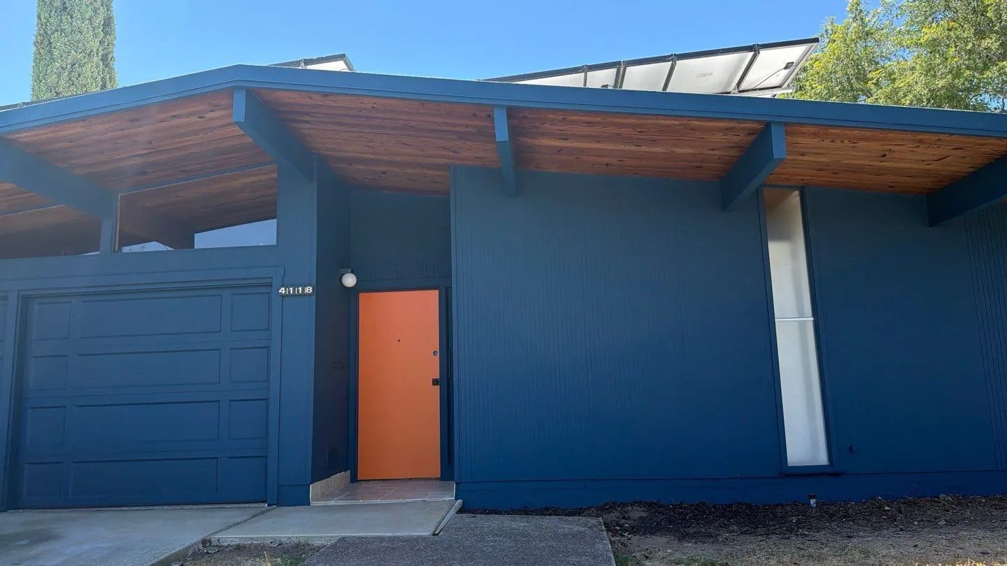 Blue Mid-Century Modern Home Exterior Deep blue mid-century modern residential home with wooden beam overhang, orange entry door, and metal garage doors