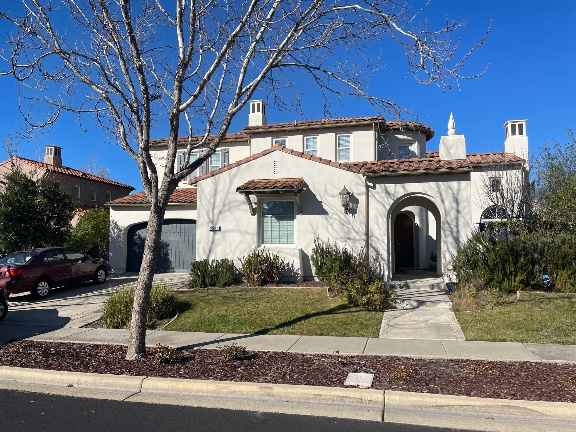 Cream Exterior Residential Home Cream-painted residential home exterior with terra-cotta tile roof, arched entry, white trim, and gray garage door.